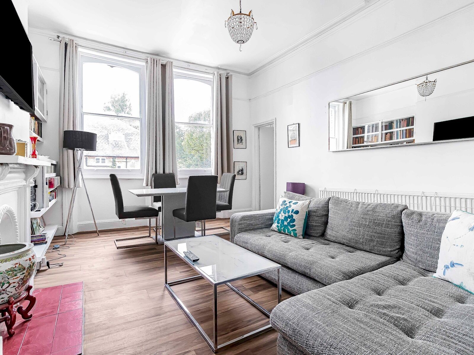 Un salon moderne avec un canapé, une table basse en verre et une table à manger avec des chaises. On y trouve également une bibliothèque, un lampadaire et un lustre.