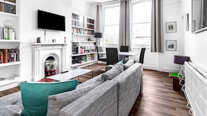 A modern living room with a fireplace, a television, a bookshelf, and a dining area. - Spacious London Flat | Near Primrose Hill & Camden - Pass the Keys (London)