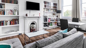 A modern living room with a fireplace, bookshelves, a flat-screen TV, and a comfortable seating area. - Spacious London Flat | Near Primrose Hill & Camden - Pass the Keys (London)