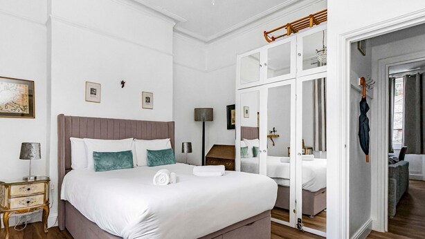 A modern hotel room with a large bed, a wooden floor, and a mirror cabinet. - Spacious London Flat | Near Primrose Hill & Camden - Pass the Keys (London)