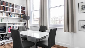 A modern room with a white table, four black chairs, a bookshelf, and a window with curtains. - Spacious London Flat | Near Primrose Hill & Camden - Pass the Keys (London)