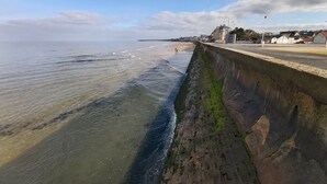 A coastal promenade with a concrete barrier, clear skies, and distant buildings.