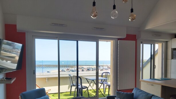 A modern living room with a large window overlooking a beach and parking area.