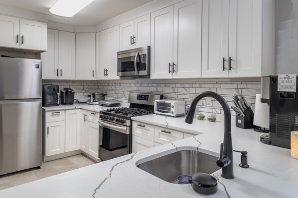 Una cocina moderna con armarios blancos, electrodomésticos de acero inoxidable, encimera de mármol y grifo negro.