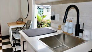 Cocina compacta con pileta, un pequeño comedor con una silla, y vista a espacios verdes.