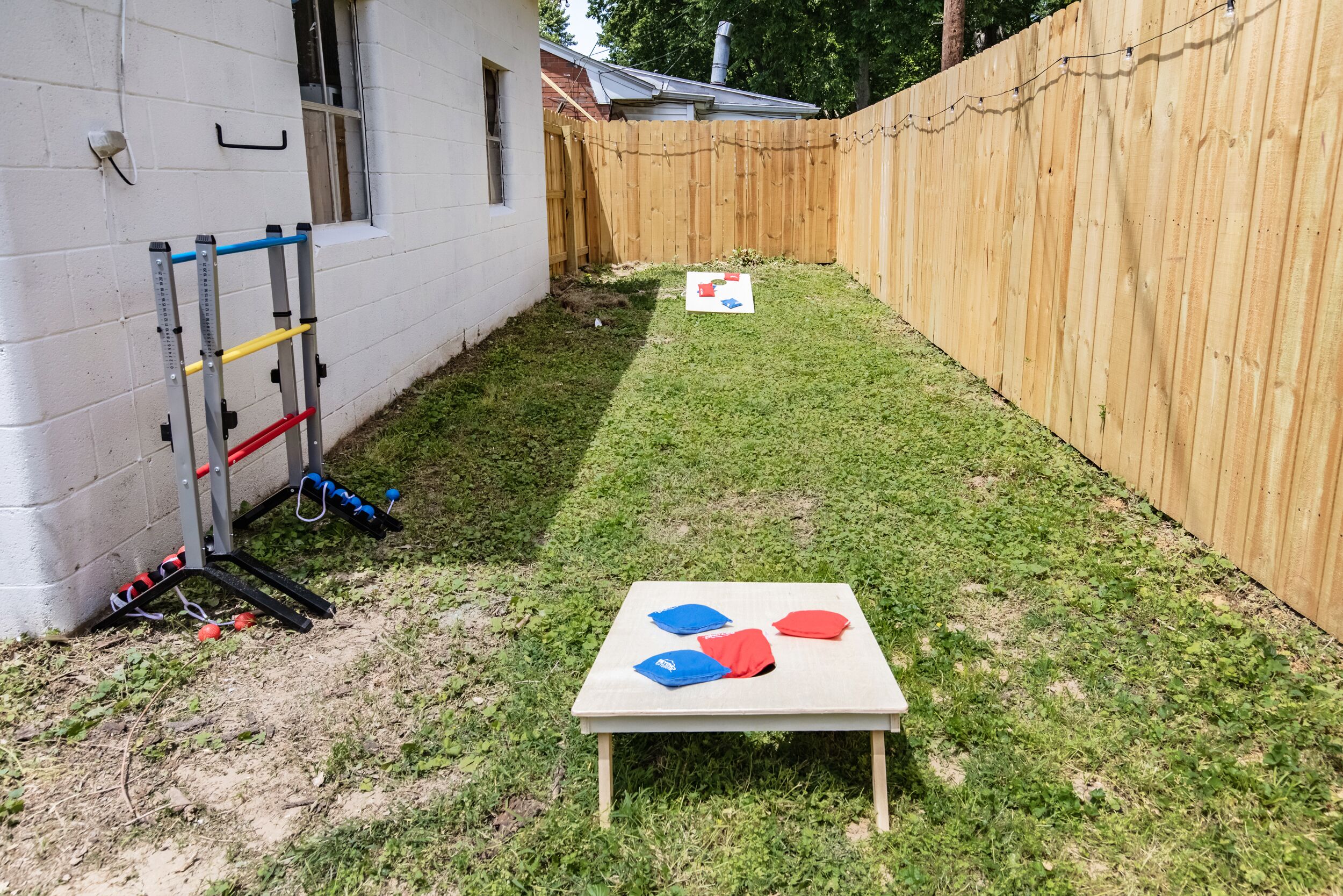 A backyard with a wooden fence, a metal exercise equipment, and a table with colored cushions.