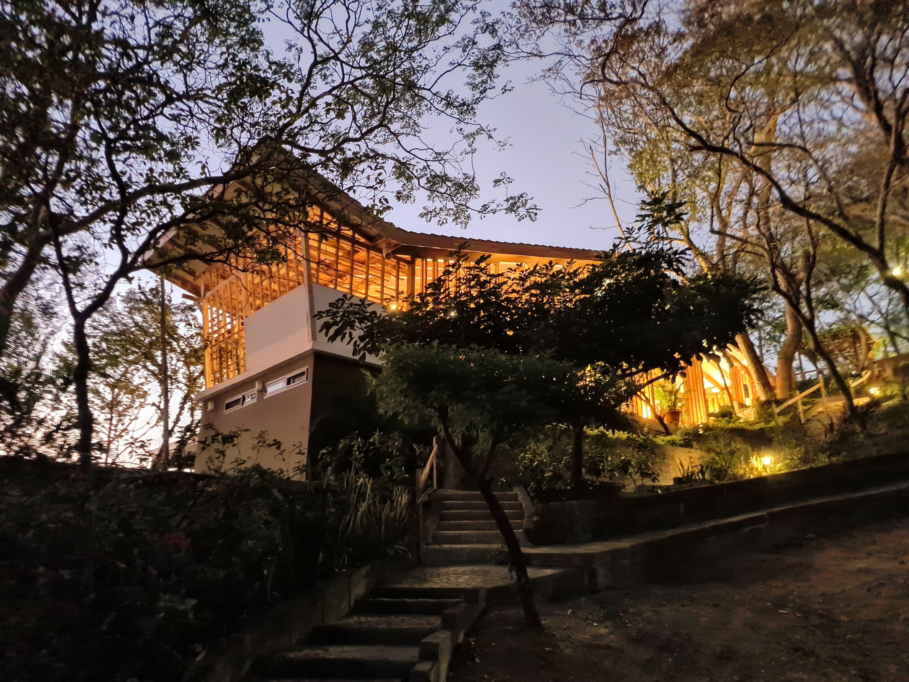 A traditional wooden structure with a modern extension, surrounded by trees and a staircase leading up to it.