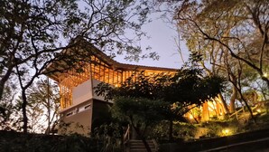 Une structure traditionnelle en bois, agrémentée d’une extension moderne, entourée d’arbres et accessible par un escalier.