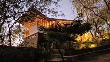 A traditional wooden structure with a modern extension, surrounded by trees and a staircase leading up to it.