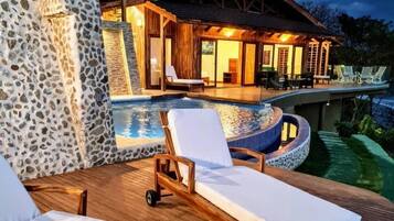 A poolside area with lounge chairs, a stone wall, and a wooden building with glass doors.