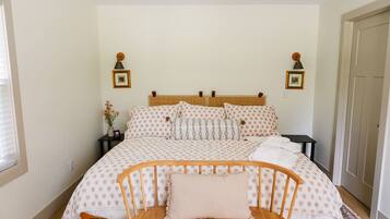 A bedroom with a bed, bedside tables, a nightstand, a chair, and a door.