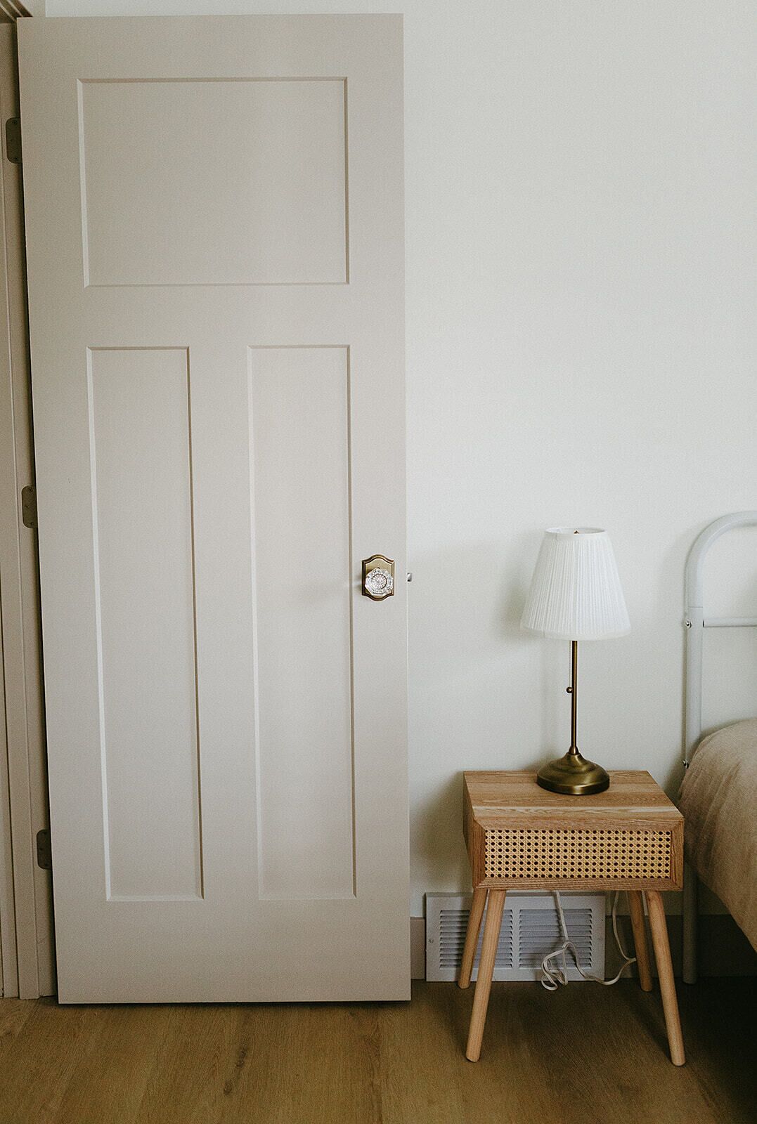 A closed door with a keyhole, a bedside table with a lamp, and a bed with a headboard.