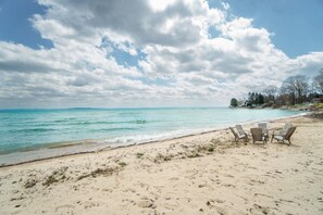Een strand met een rij stoelen gericht op de oceaan, een heldere lucht en een verre kustlijn met bomen.