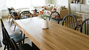 Een eethoek met een houten tafel, zwarte stoelen, een geweven hanglamp en een bloemenvaas.