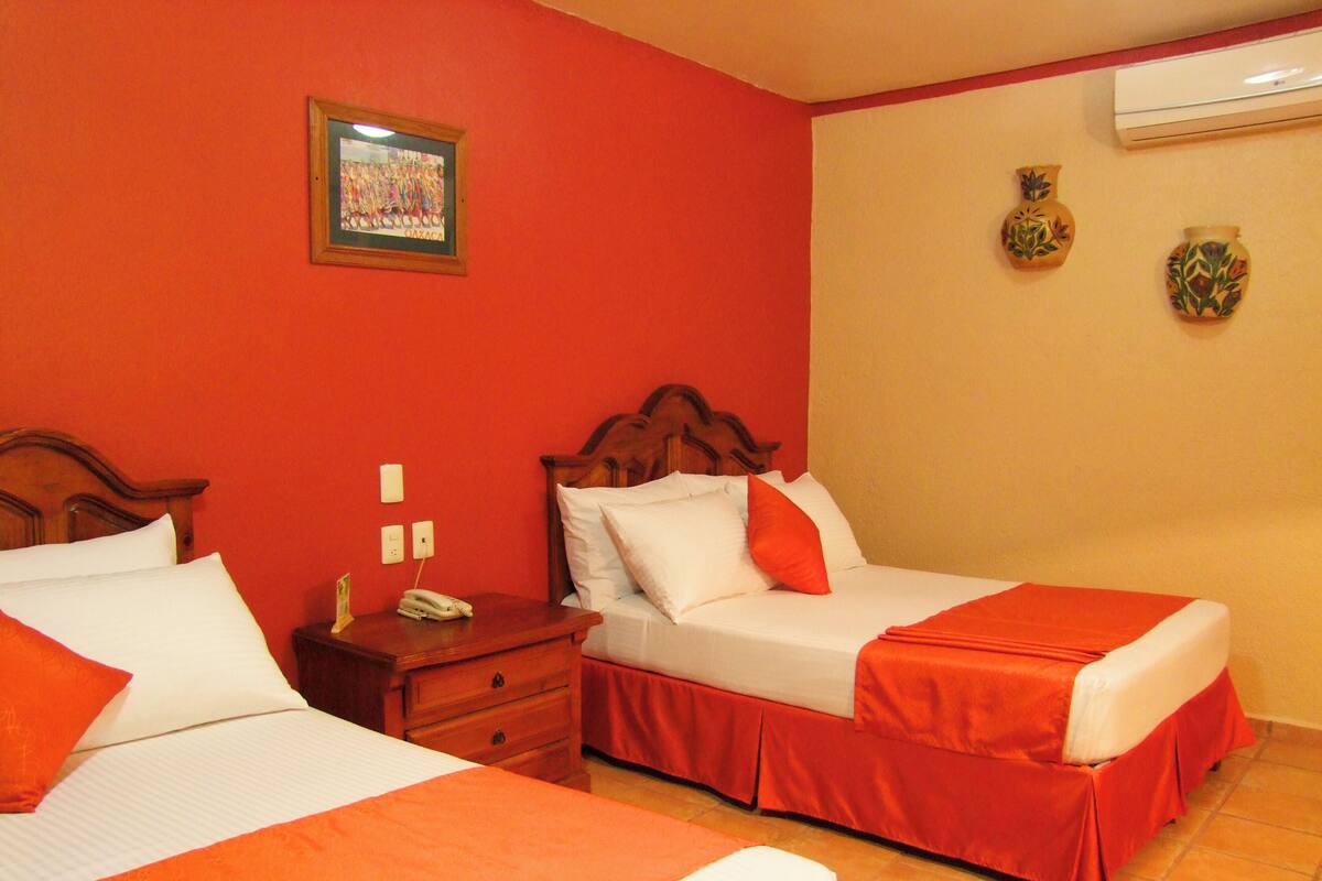 Ein Hotelzimmer mit zwei Betten, roten Wänden, einem Holz-Kopfende, einem Nachttisch und einem gerahmten Bild an der Wand.