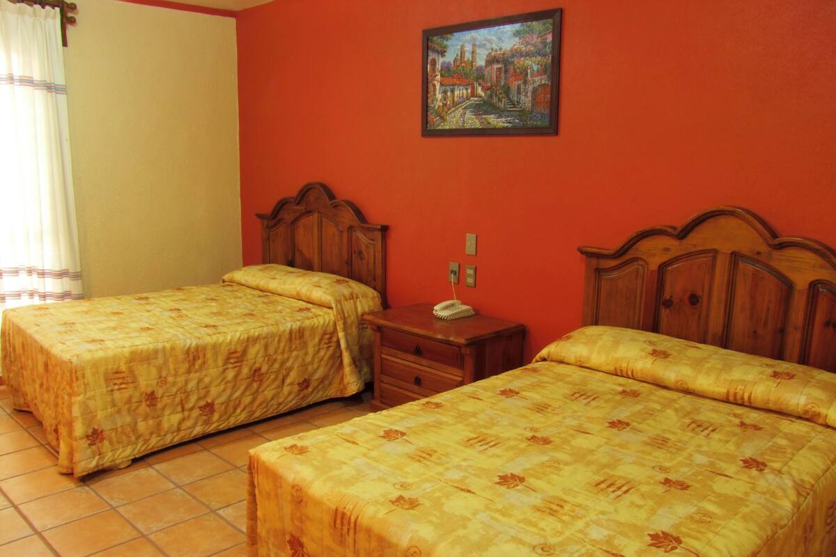 Ein Hotelzimmer mit zwei Einzelbetten, einem Holznachttisch, einem Telefon und einem Gemälde an der Wand.