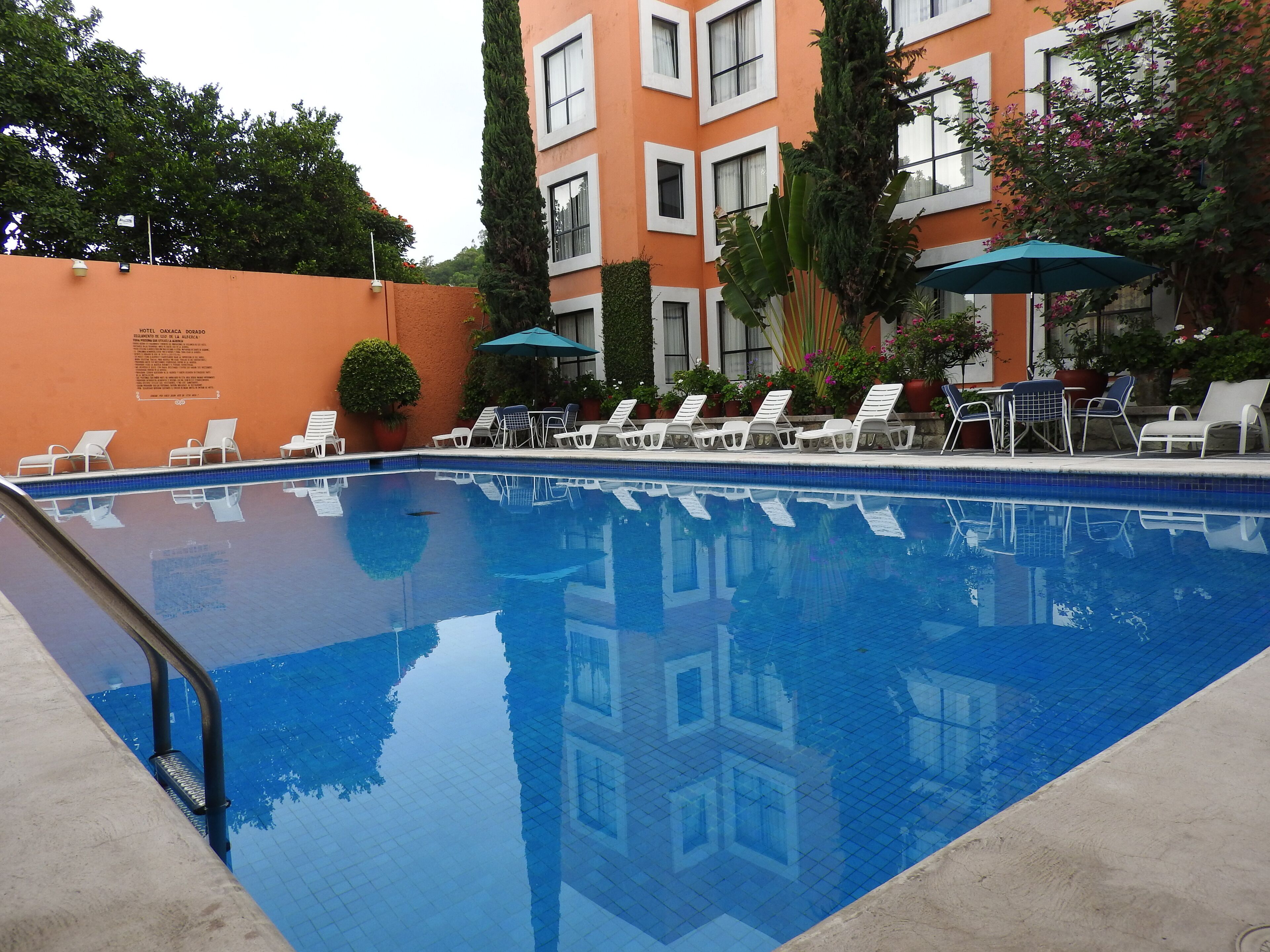 Una piscina con lettini e ombrelloni, circondata da un edificio con numerose finestre e un cartello.