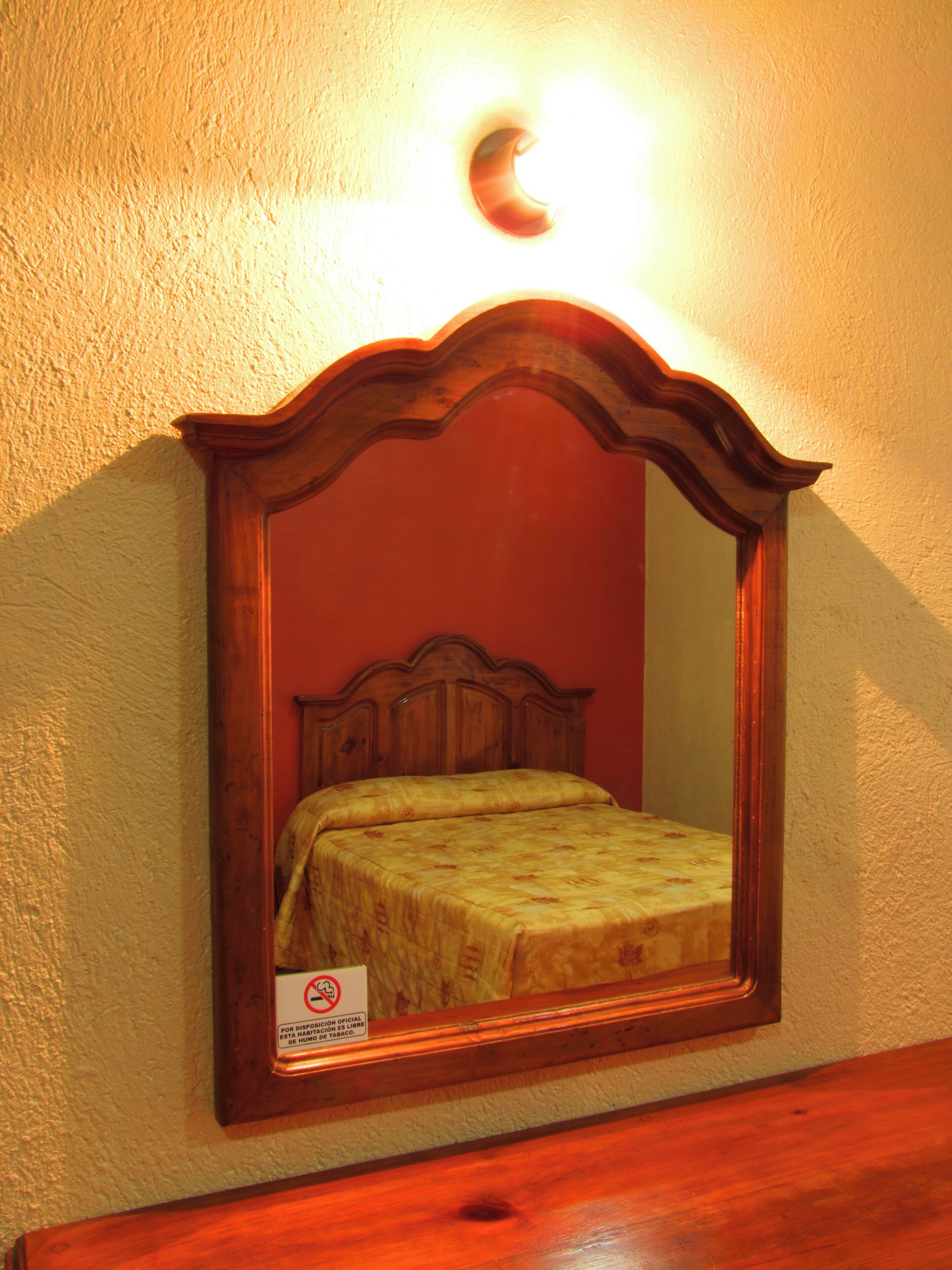A bedroom with a wooden headboard, a bed with a floral bedspread, and a wall-mounted mirror.