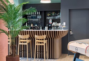 A bar area with a curved counter, two stools, a potted plant, and a surfboard.