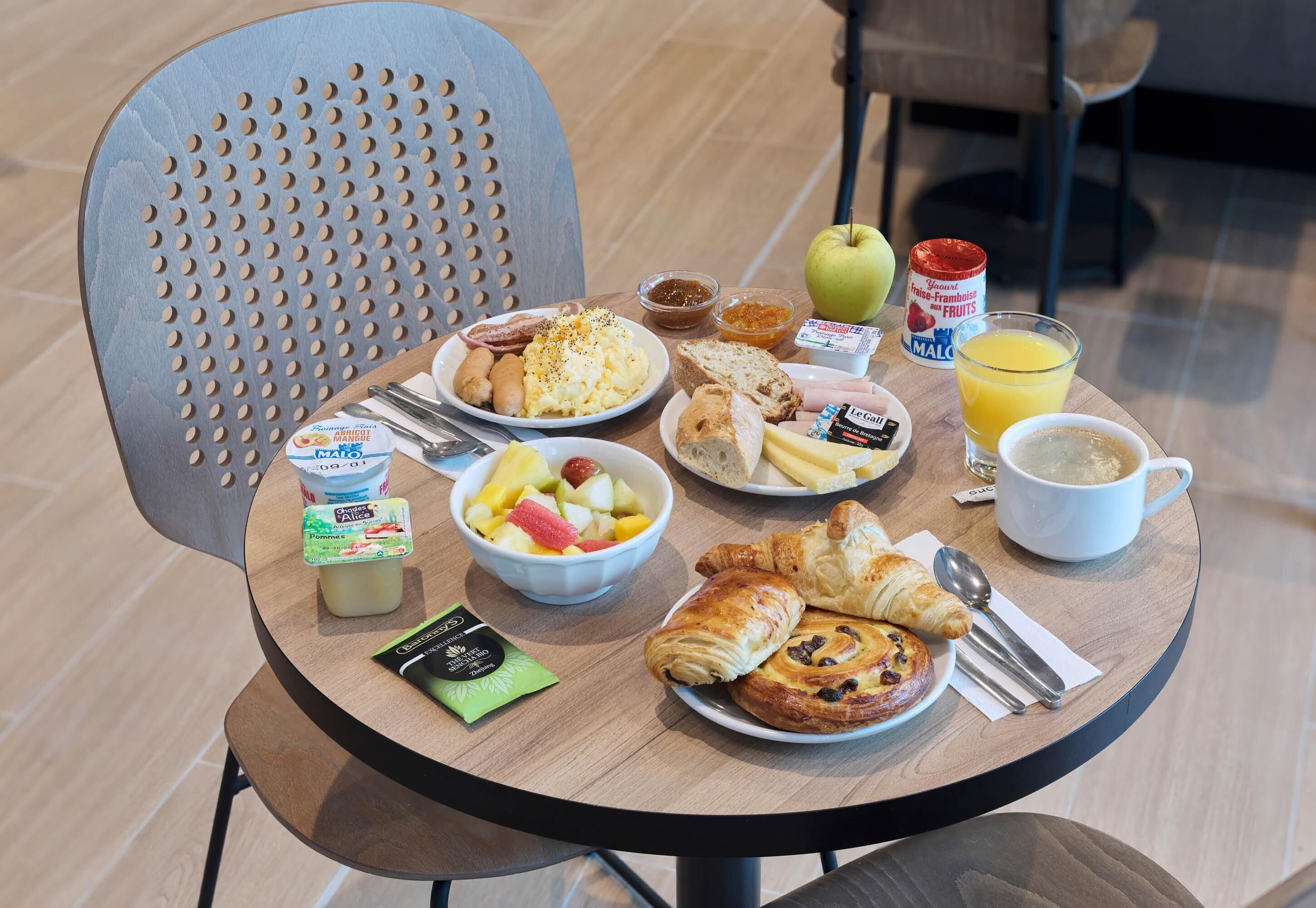 A breakfast table with various food items, a cup of coffee, and a fruit bowl.