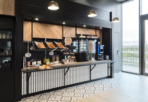 A modern cafe with a counter displaying pastries, a coffee machine, and a refrigerated display.