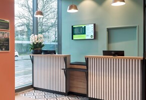 A reception desk with a digital display, a potted plant, and a view of the street outside.