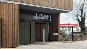 A building entrance with a sign indicating parking directions and a fuel station in the background. - B&B HOTEL Versailles Rocquencourt (Le Chesnay-Rocquencourt)