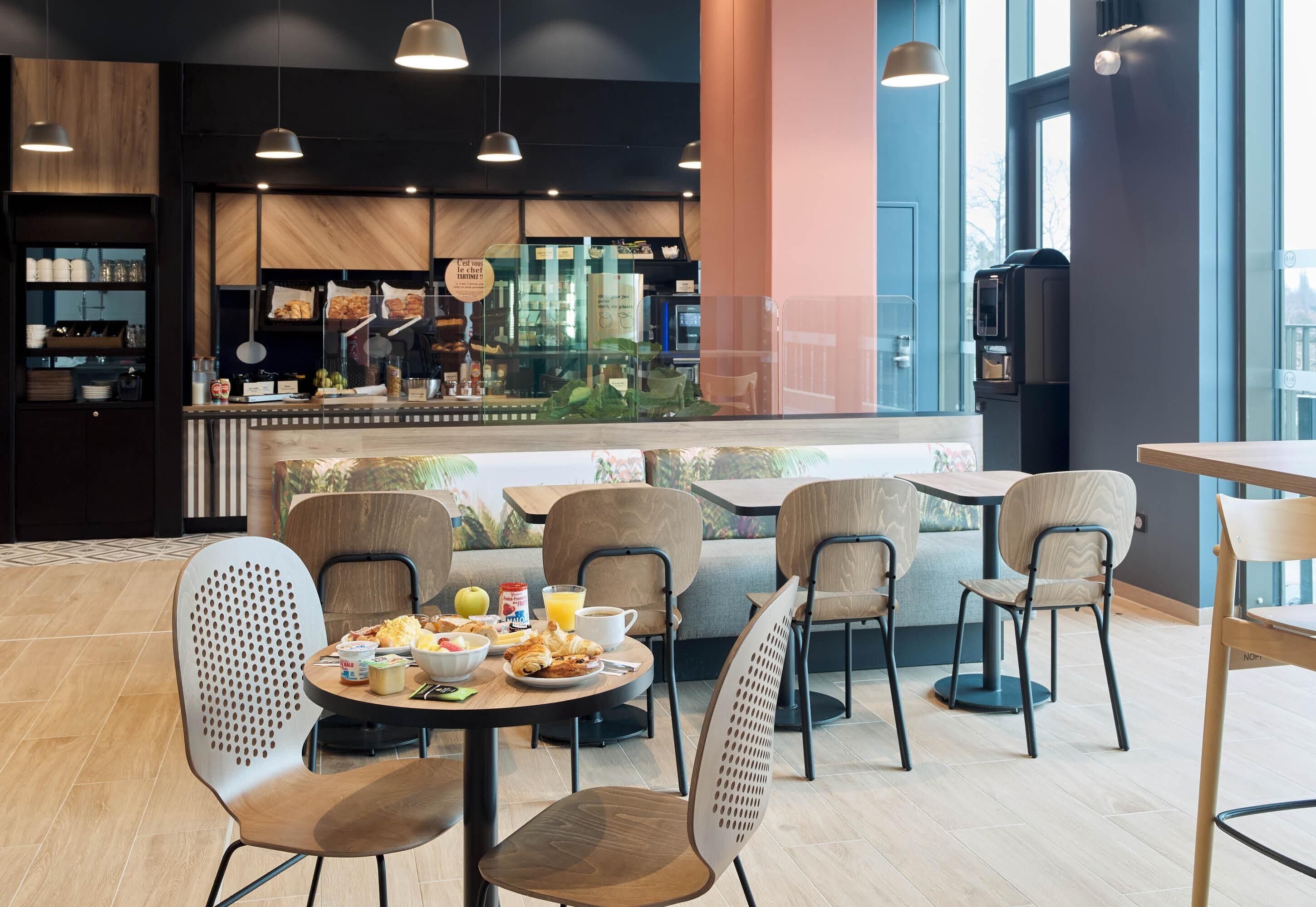 Um café moderno com mesas e cadeiras redondas, um balcão com um chef e vista para a cidade.