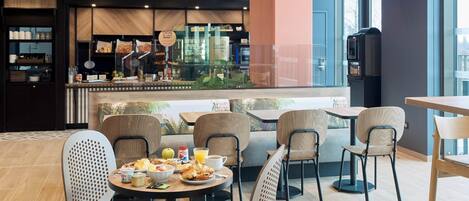 Um café moderno com mesas e cadeiras redondas, um balcão com um chef e vista para a cidade.