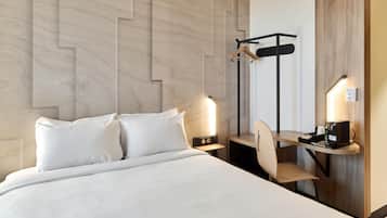 A hotel room with a bed, bedside tables, a desk with a chair, a coat rack, and a wall-mounted light fixture.