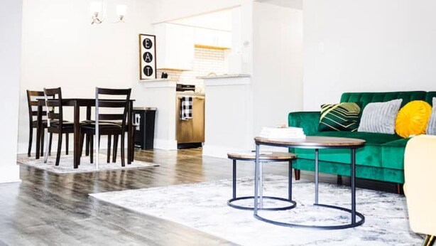 Un soggiorno moderno con un divano verde, un'area pranzo con sedie in legno e una cucina sullo sfondo.