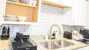 Cucina con mobili bianchi, piano di lavoro in granito, lavello in acciaio inossidabile e scolapiatti.