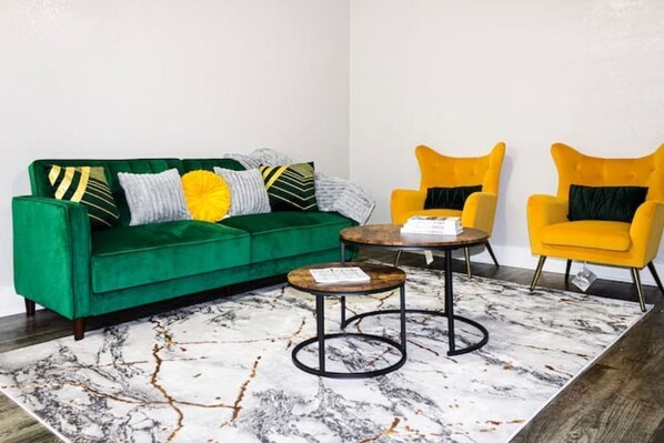A green sofa with multiple pillows, two yellow armchairs, and a small round table with a book on it.