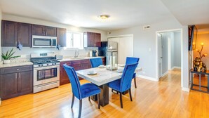 A modern kitchen with dark cabinets, stainless steel appliances, and a dining area with blue chairs and a white table. - Walk to Train & Bus: Updated Chicago Apartment (Chicago)