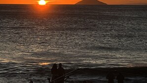 A sunset over the ocean with a silhouette of a mountain in the distance.