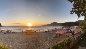 A beach with umbrellas and people, a sunset, and hills in the background.