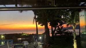 A sunset view from a balcony with a pool, chairs, and a table.
