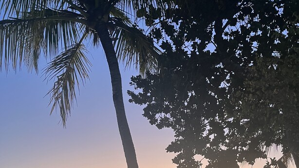 A patio with wicker furniture, overlooking a beach at sunset.