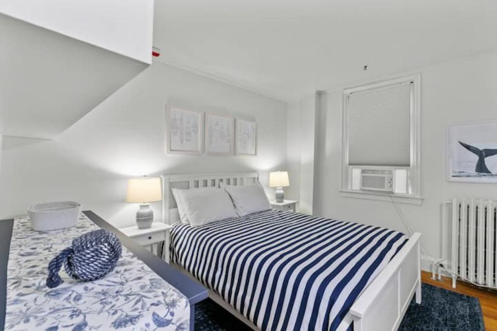 A bedroom with a bed, bedside tables, a lamp, a radiator, and framed pictures on the wall.