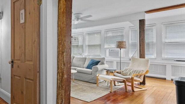 A room with a wooden floor, a white sofa, a chair with a cushion, and a ceiling fan.