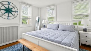 A bedroom with a large bed, white walls, a compass wall decoration, and a window with blinds.