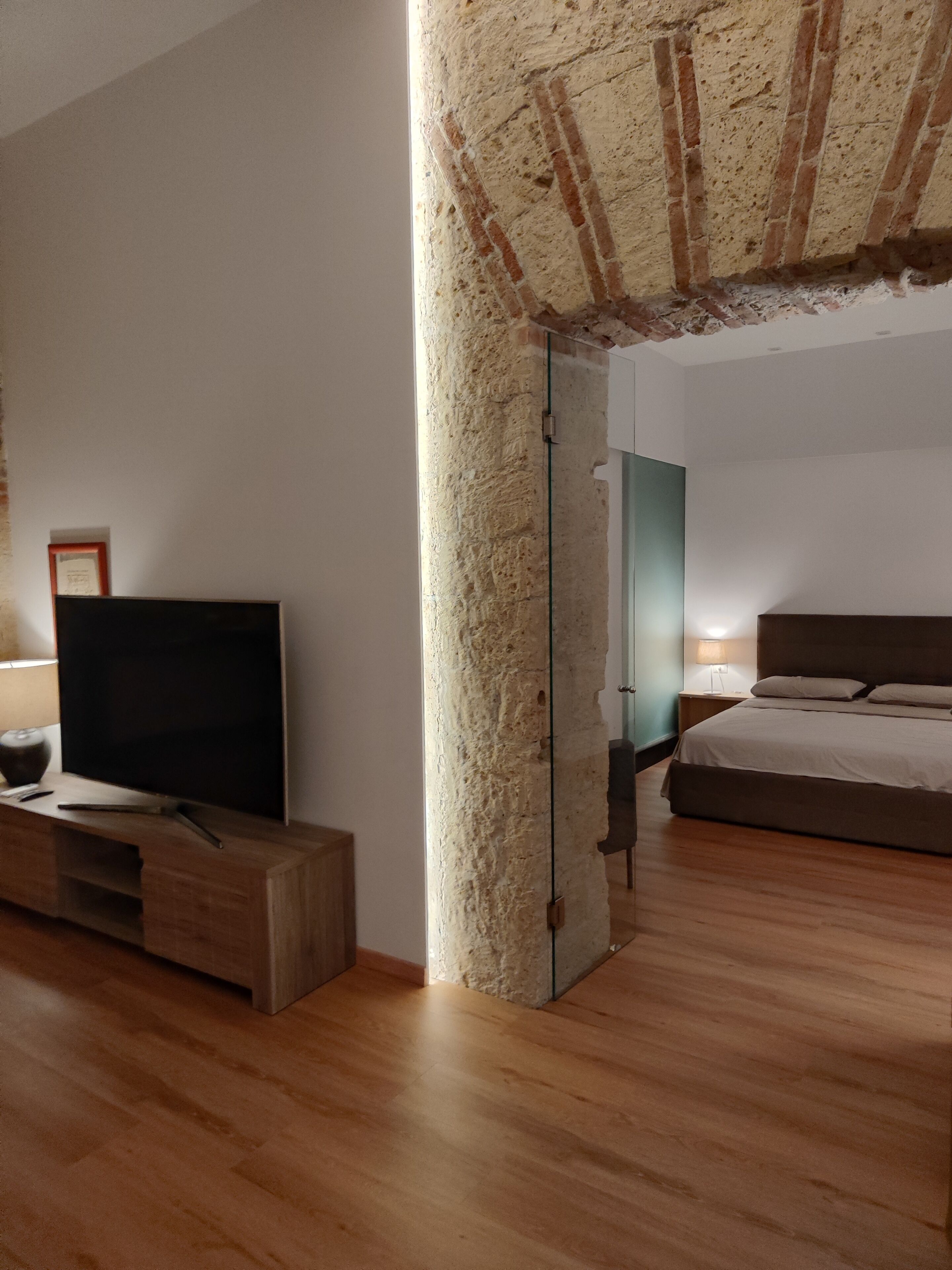 A modern bedroom with a large bed, a television on a wooden stand, and a stone pillar.