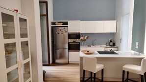 A modern kitchen with white cabinets, a stainless steel refrigerator, a built-in oven, and a small island with bar stools. - Suite in the historic center of Naples (Napoli)
