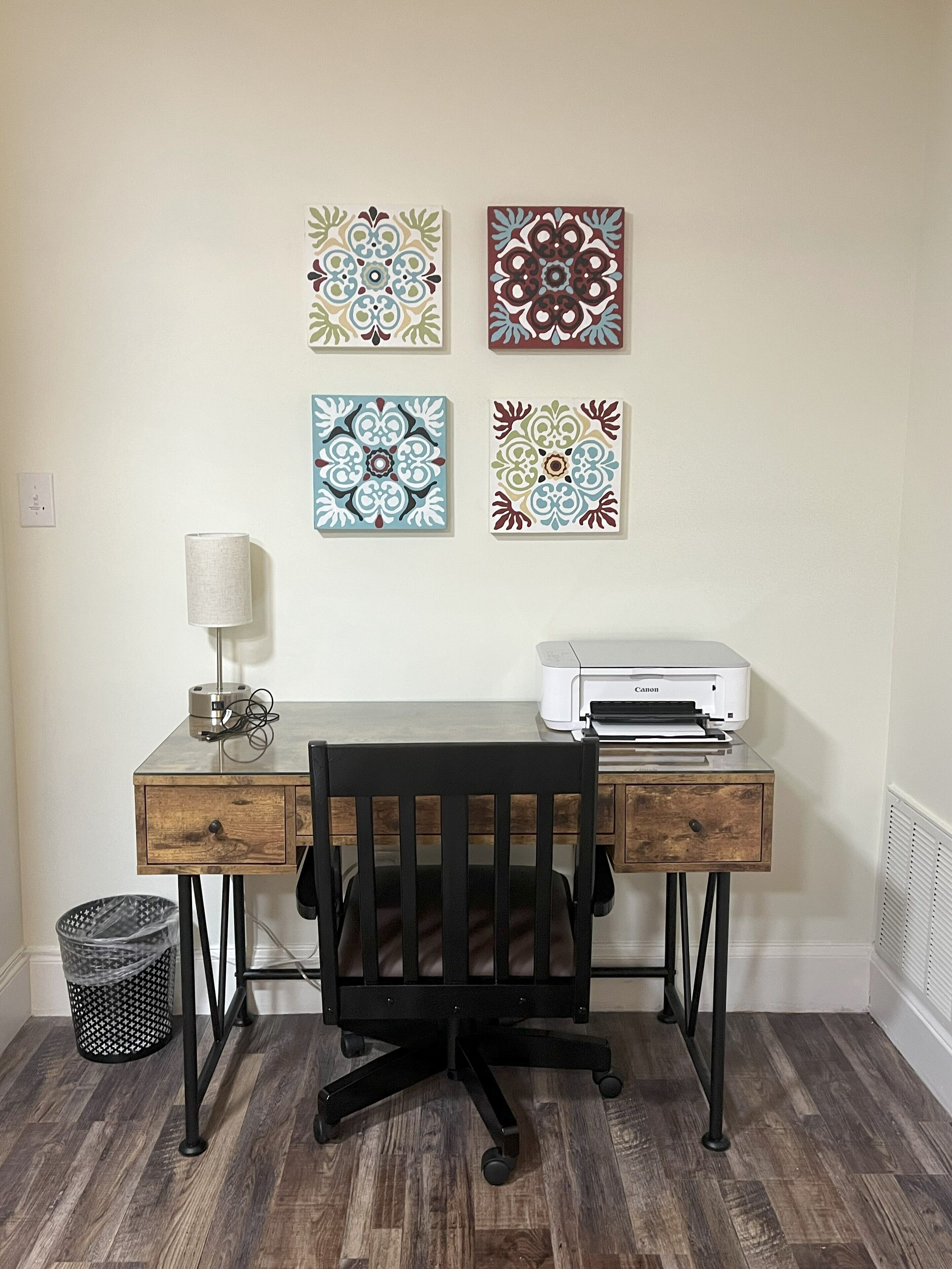 A workspace with a desk, chair, printer, lamp, and decorative tiles on the wall.