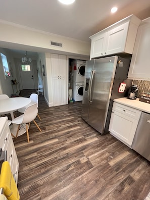 A modern kitchen with stainless steel appliances, a dining area with white chairs, and a laundry area with stacked washers and dryers. - Family Friendly 3 bedroom close to downtown Raleigh (Raleigh)