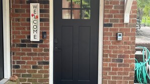 A black door with a welcome mat and a welcome sign on a brick wall. - Family Friendly 3 bedroom close to downtown Raleigh (Raleigh)