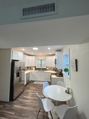 A modern kitchen with white cabinets, a stainless steel refrigerator, and a dining area with a white table and chairs. - Family Friendly 3 bedroom close to downtown Raleigh (Raleigh)