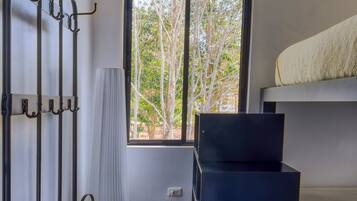 Un dormitorio con literas, un escritorio con computadora, una ventana con vista a árboles y un equipo de aire acondicionado instalado en la pared.