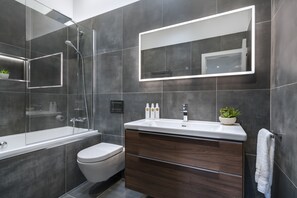 A modern bathroom with a glass-enclosed shower, a white toilet, a wooden vanity with a mirror, and a small potted plant. - NEW - Mayfair House - 5 Star - Lake View Luxury (Bowness-on-Windermere)