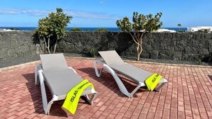 Zwei Liegestühle mit 'ISLAS STARS' Handtüchern auf einer Ziegelterrasse mit Blick auf den Ozean.